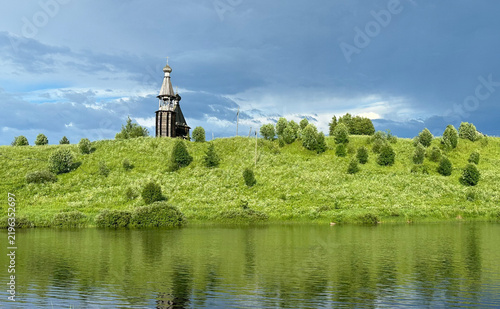 Traditional Wooden Church on a Grassy Hill Overlooking a Calm River Under a Dramatic Sky