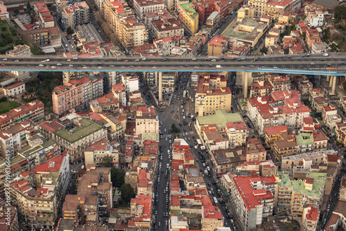 Aerial view of the dense urban landscape of Naples with its characteristic red-tiled rooftops and a prominent elevated highway bridge crossing the city in Naples, Campania, Italy.