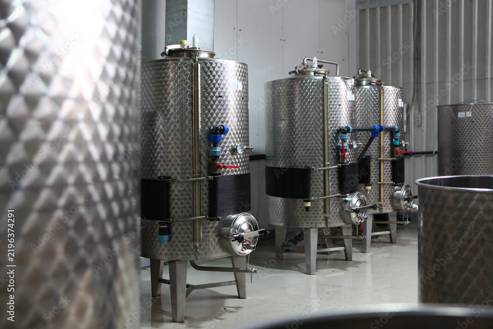 Obraz premium Containers for wine wort. Fermentation tank. Industrial winery interior with stainless steel tanks. Blue valves and round manholes. Concept of small modern winery