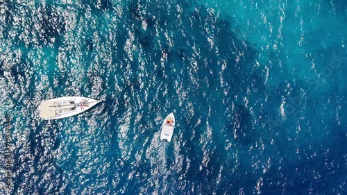 Aerial view of motorboat navigating through vibrant blue sea waters, surrounded by waves and other boats, showcasing a serene resort atmosphere in a tropical coastal region