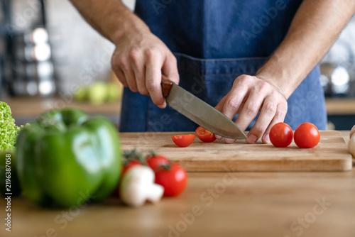 Cropped shot of man cooking in modern kitchen with fresh vegetables on table, preparing healthy homemade meal, culinary lifestyle concept, food preparation process and everyday home activity