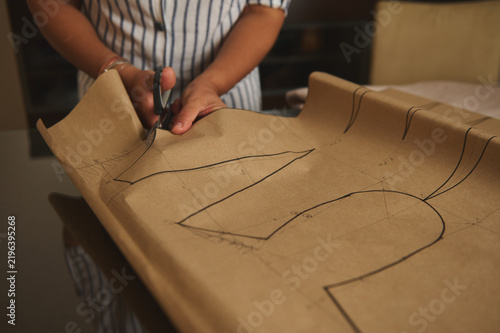 Woman cutting dress pattern on brown paper with scissors for sewing and dressmaking project