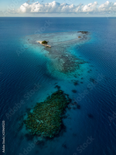 Aerial view of Tikehau atoll featuring vibrant coral reefs, turquoise lagoon waters, and a small motu surrounded by the deep blue Pacific Ocean in the Tuamotu and Gambier Islands, French Polynesia.
