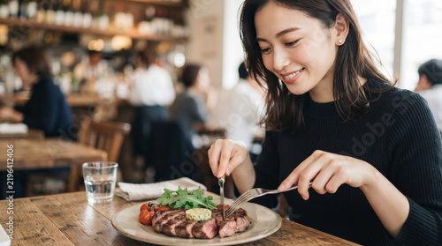 レストランでステーキを笑顔で食べる若い女性の食事風景
