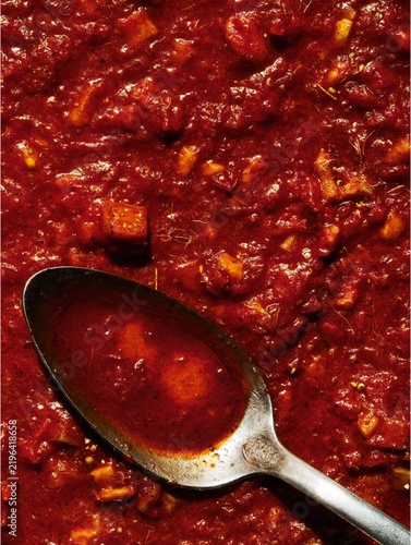 Chunky tomato sauce with herbs and metal spoon, macro food texture