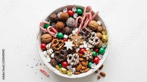 Top-down view of a festive white bowl filled with assorted Christmas candies, chocolates, nuts, and cookies, perfect for holiday celebrations
