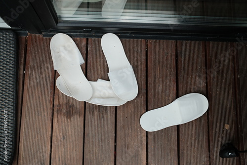 Obraz na płótnie Several white guest slippers rest on the wooden floorboards outside near a glass door at daylight, suggesting someone stepped out briefly to enjoy the view or fresh air area
