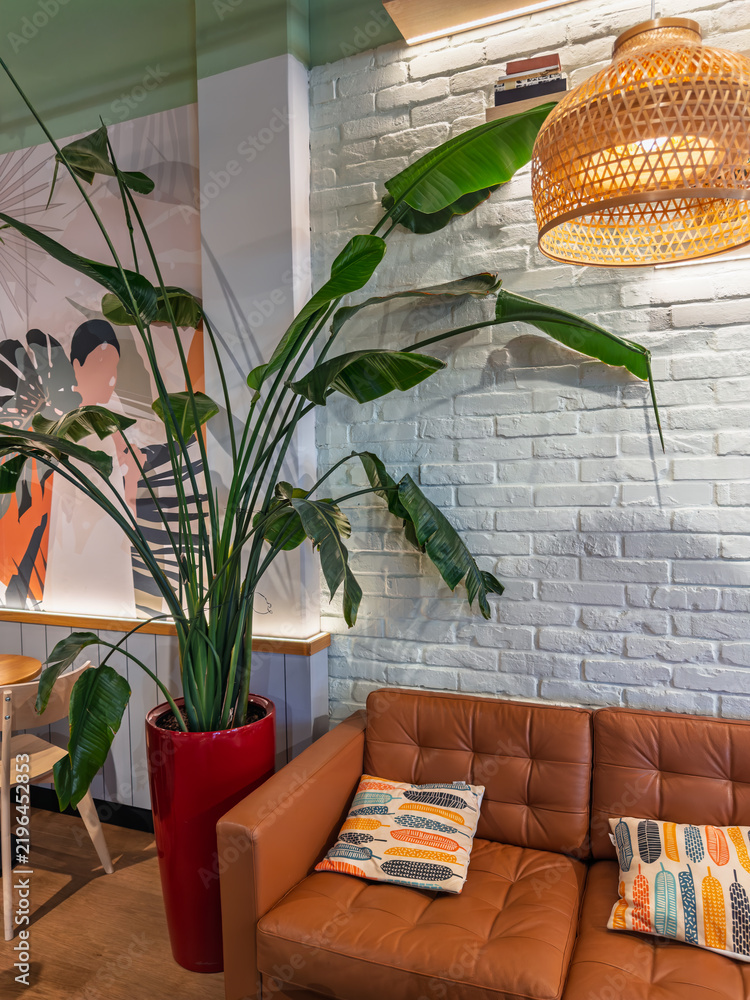 Obraz premium Stylish Modern Cafe Interior Corner with Large Strelitzia Plant and Leather Sofa