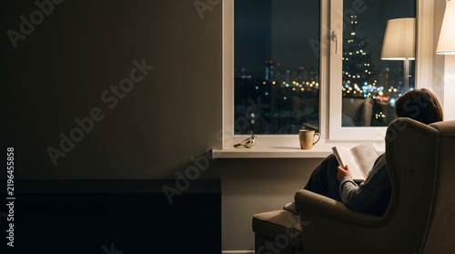 Person relaxing in an armchair and reading a book at night  