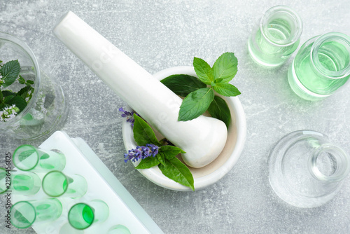 Foto Mortar with pestle, fresh herbs and glassware on grey table, flat lay