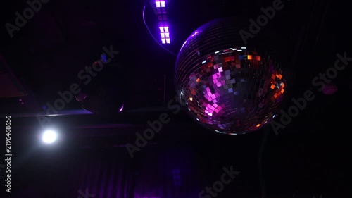 Shiny disco mirror ball reflecting vibrant purple and pink stage lights in dark nightclub, creating festive party atmosphere for dance music entertainment celebration