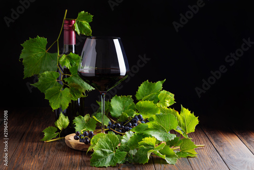 Obraz na plátně Full glass of red wine bottle and fresh grapes with vine leaves on wooden table