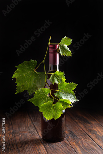 Fotografie Single bottle of dark red wine adorned with fresh green grape leaves on a wooden