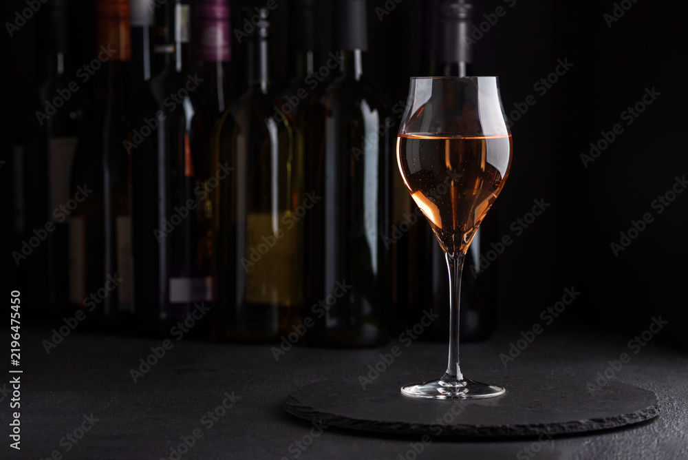 Fototapeta premium Rose wine in elegant glass with bottles in background and dark moody lighting