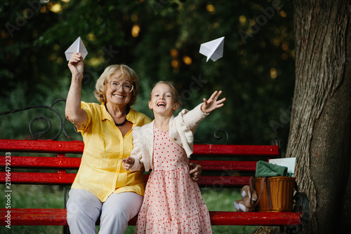 Obraz na płótnie Happy grandmother granddaughter launching paper airplanes in park