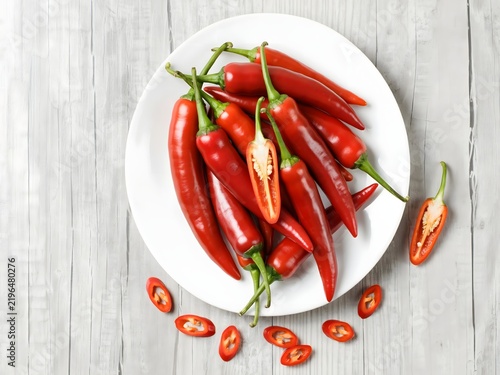 Fresh red chili peppers arranged on white plate with sliced peppers for culinary and food blog use