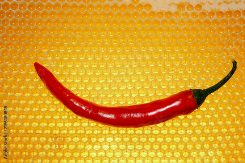 A red hot chili pepper pod set against golden honeycombs. A concept featuring spicy honey seasoning, gourmet ingredients, and contrasting flavors.