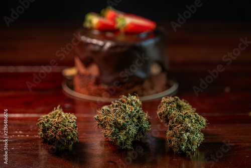 Chocolate strawberry fruit brown cake wooden table with marijuana flower blooms