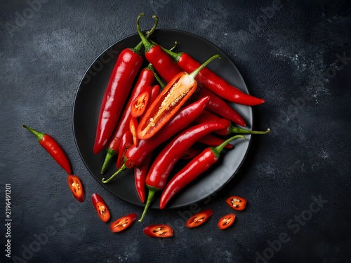 Assorted fresh chili peppers arranged on black plate with scattered smaller peppers for culinary presentation