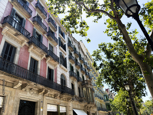 Sunlit historic architecture with wrought iron balconies and Gucci storefront on a tree lined street in Barcelona, Spain