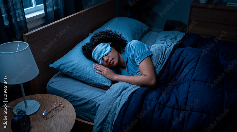 Fototapeta premium Young woman sleeping peacefully in bed at night wearing a comfortable blue sleep eye mask cover