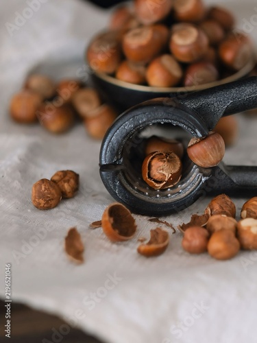 Cuadro en lienzo Metal nutcracker cracking a hazelnut with shell fragments, rustic dark food photography setup with linen background
