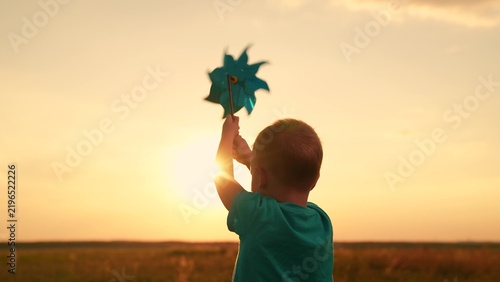 Child childhood. Family outing, nature. Kid boy runs through summer field holding toy pinwheel, sunny day. Happy child plays with toy pinwheel outdoors. Child nature. Child son, dream in park sunset