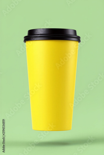 Bright yellow takeaway coffee cup with black snap-on lid floating against a pastel green background, minimalist beverage packaging mockup, copy space