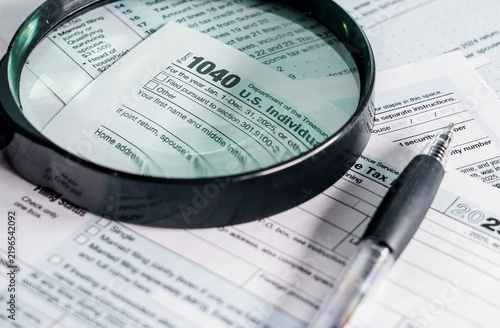 Magnifying glass and pen over US individual income tax form 1040 for tax season preparation and filing