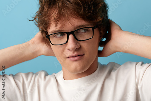 Foto Young man in glasses shows skeptical sideways glance with narrow eyes and tight mouth, hands behind head