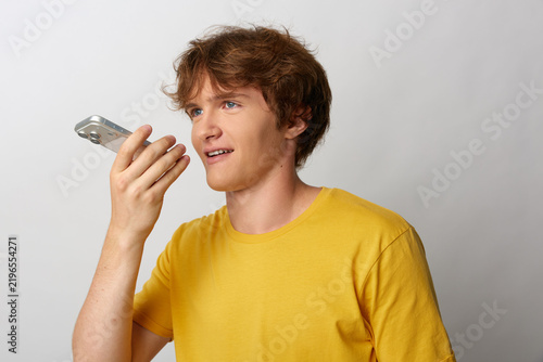 Bild auf Leinwand Young man in yellow t-shirt talking into smartphone speakerphone, profile view, smiling in friendly conversation
