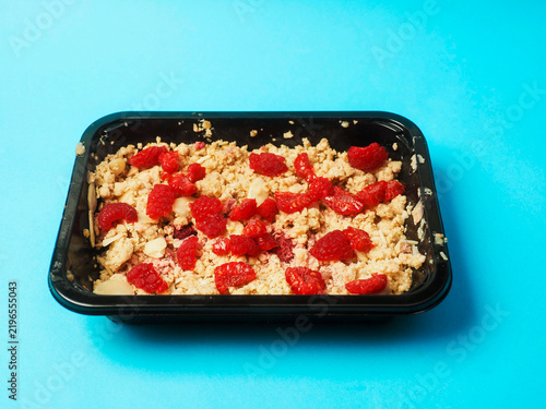 Fotografie Freshly baked crumble topped with sliced strawberries in a black baking dish on blue background