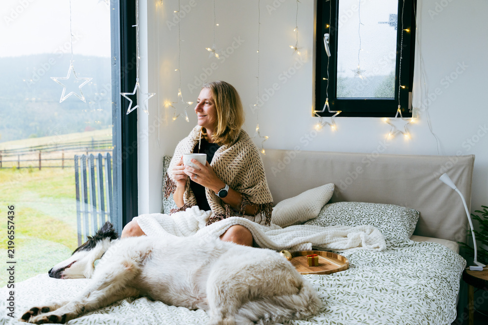 Naklejka premium happy woman with dog relaxing in bed at Christmas time