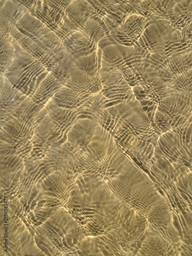 Top down close up background of golden sun caustics and light water ripples on a shallow sandy sea floor in Jurmala.