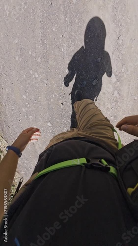 Vertical video of hiker walking a dirt trail with a backpack and walking stick, showing shadowed silhouette.