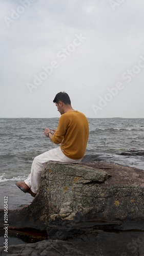 Man Sitting on a Helsinki Beach Looking at His Phone on a Cloudy Day