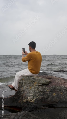 Man Sitting on the Beach Taking Photos With His Smartphone