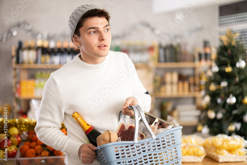 While shopping before new year, guy in winter hat walks through grocery store, studies windows, looks for something in store, spending time in moll shopping center.