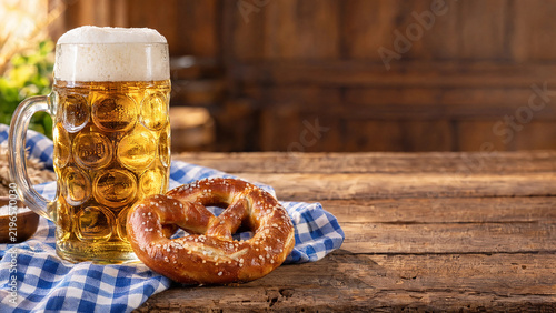 Tall beer stein beside a soft pretzel on a blue and white checked cloth