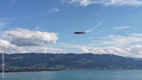 Modern passenger airship flying above Lake Constance with scenic alpine foothills, blue water and dramatic clouds in southern Germany.