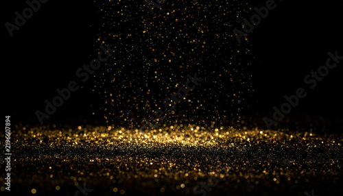 Golden glitter particle cloud above reflective black surface with sparkling dust and warm bokeh light creating elegant festive background