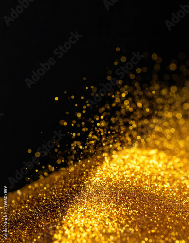Golden glitter particle cloud on dark background creates sparkling abstract texture with glowing dust and rich metallic color