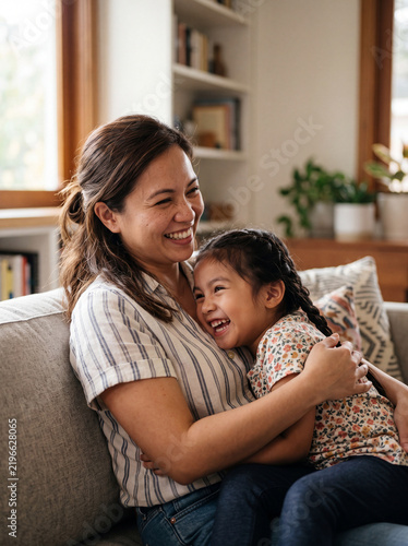 Filipino Mother and Child daughter hugging vertical portrait of happy family laughing on living room sofa