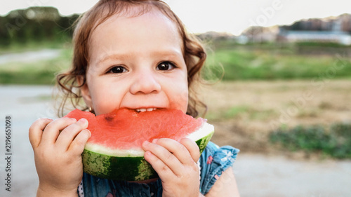 Child toddler eating watermelon in city park during summer vacation - Focus on hands holding fresh fruit - UGC concept