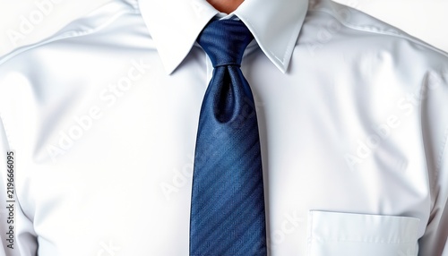 A close up view of an individual wearing a white shirt with rolled up sleeves, a dark tie with a blue pattern, and a light blue shirt underneath