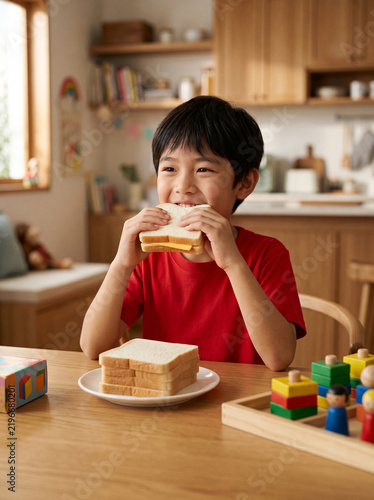 Cheerful Asian child taking a big bite of a delicious cheese sandwich at home
