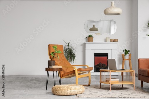 Interior of light living room with stylish mirror, armchair and fireplace