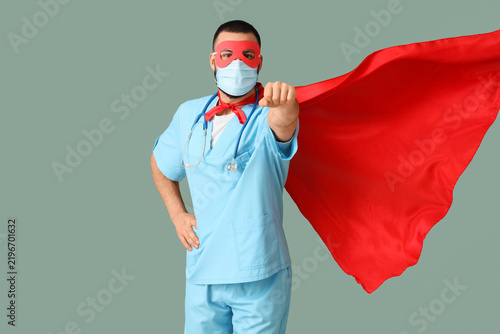 Male doctor dressed as superhero with medical mask on green background