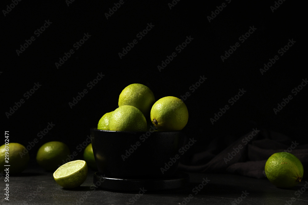 Obraz premium Bowl with fresh ripe limes on black background