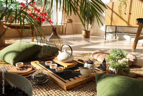 Tray with Asian tea set and pillows on carpet in room